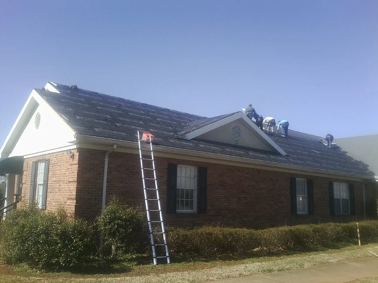 Crew tearing shingles off a brick ranch roof with a ladder set — Metal Roof Repair work by our crew in Waterford